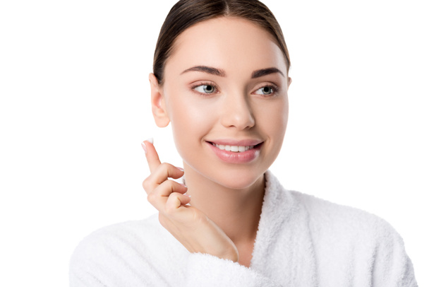 schöne lächelnde Frau im Bademantel mit Gesichtscreme auf der Hand isoliert auf weiß - Foto, Bild