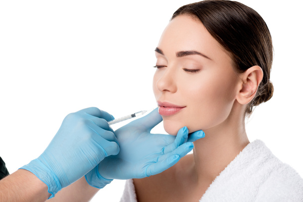 Doctor in de latex handschoenen lip injectie met spuit geven aantrekkelijke vrouw geïsoleerd op wit - Foto, afbeelding