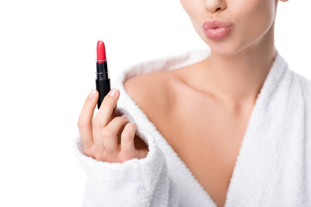 vista recortada de la mujer en albornoz haciendo pucheros labios y sosteniendo lápiz labial rojo aislado en blanco
 - Foto, Imagen