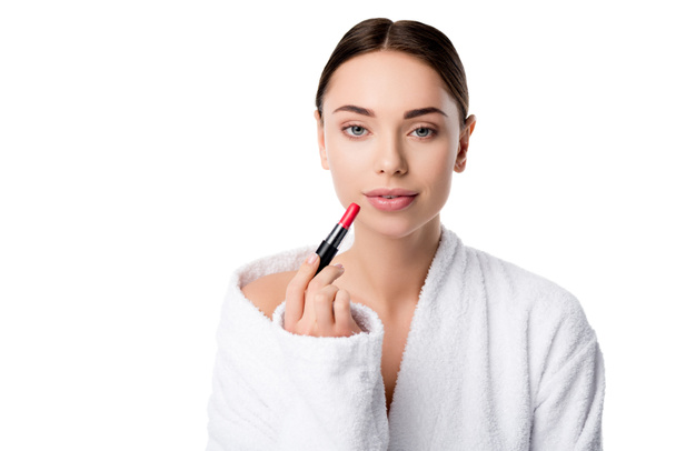 beautiful woman in bathrobe holding red lipstick and looking at camera isolated on white - Foto, Imagem