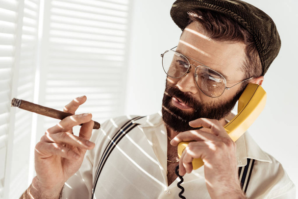 hombre barbudo en gafas y gorra hablando por teléfono y sosteniendo cigarros
  - Foto, Imagen