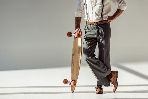 cropped view of stylish man holding longboard on grey background - Foto, immagini