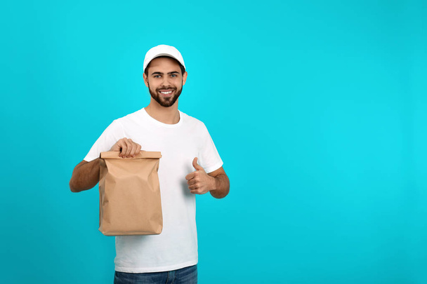 Young courier with paper bag on color background, space for text. Food delivery service - Valokuva, kuva