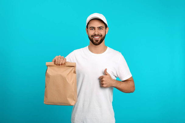 Young courier with paper bag on color background. Food delivery service - Foto, Bild