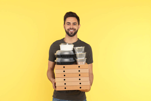 Young courier with different orders on color background. Food delivery service - Fotó, kép