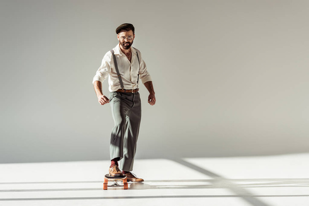 handsome bearded man riding longboard and looking at camera on grey background - Фото, изображение