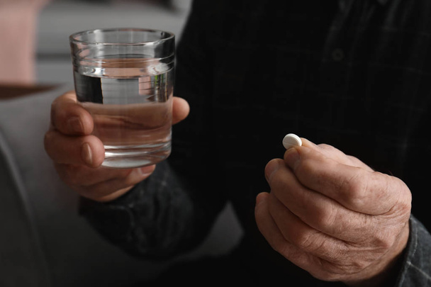 Senior man holding pill and glass of water, closeup - Photo, Image