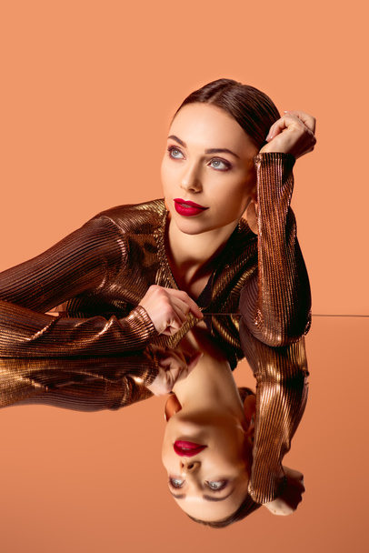 beautiful woman in golden clothes with glamorous makeup and mirror reflection isolated on orange - 写真・画像
