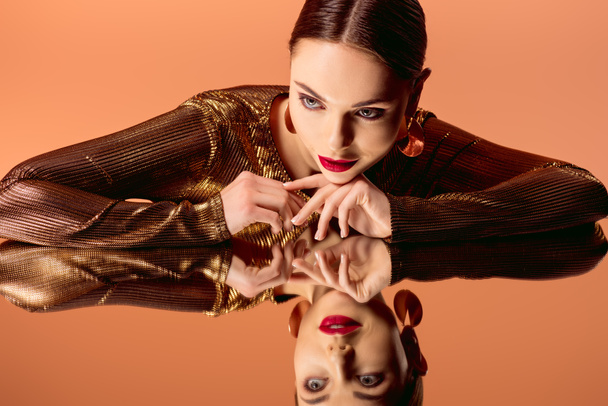 beautiful woman in golden clothes with glamorous makeup and mirror reflection posing isolated on orange - Φωτογραφία, εικόνα