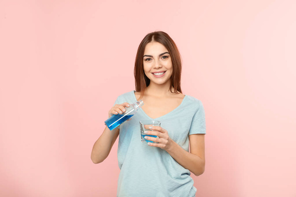 Beautiful woman pouring mouthwash from bottle into glass on color background. Teeth and oral care - Φωτογραφία, εικόνα