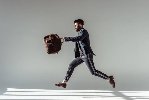 handsome bearded man with brown bag jumping on grey background - 写真・画像