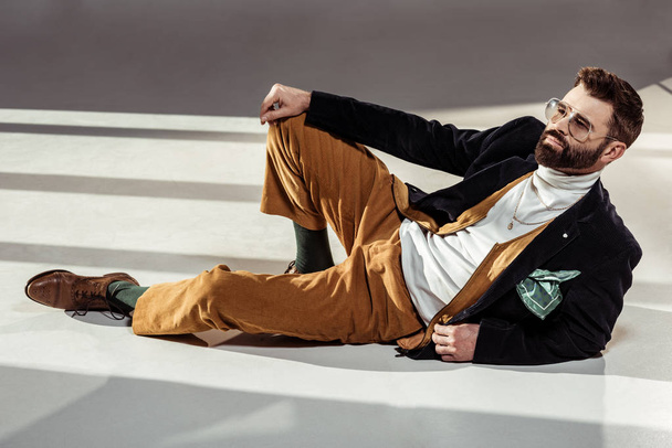 handsome stylish bearded man in glasses lying on floor - Фото, зображення