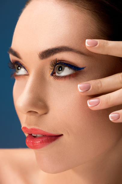 Portret van mooie vrouw met glamoureuze make-up aanraken van gezicht geïsoleerd op blauw - Foto, afbeelding