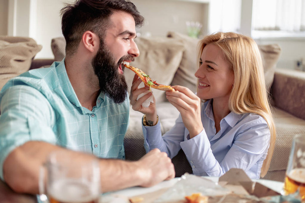 Happy couple enjoying  at home and eating pizza. - Фото, зображення