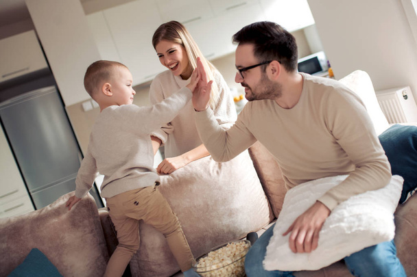 Boldog család, apa, anya és fia, ül a kanapén, és eszik popcorn otthon. - Fotó, kép