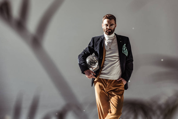 selective focus of bearded man holding mosaic disco ball and looking at camera on grey background - Foto, Imagen