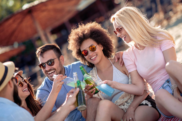 Group of attractive young people enjoying at beach, drinking and toasting. - Photo, Image
