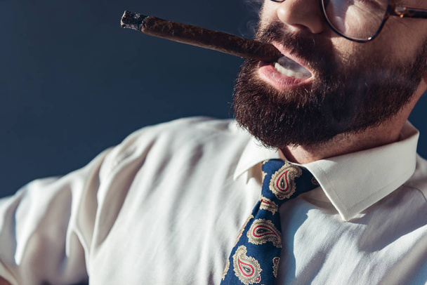 cropped view of bearded man in glasses smoking on grey background - Photo, Image