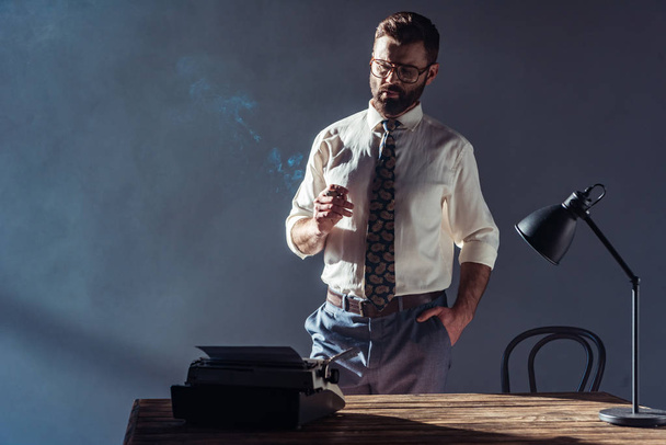 przystojny mężczyzna stojący w pobliżu tabeli i patrząc na maszynie do pisania - Zdjęcie, obraz