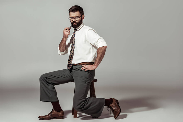 handsome bearded man with pipe sitting on chair and looking at camera - Fotoğraf, Görsel