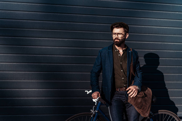 handsome bearded man in glasses and cap holding bag and bicycle - Fotografie, Obrázek