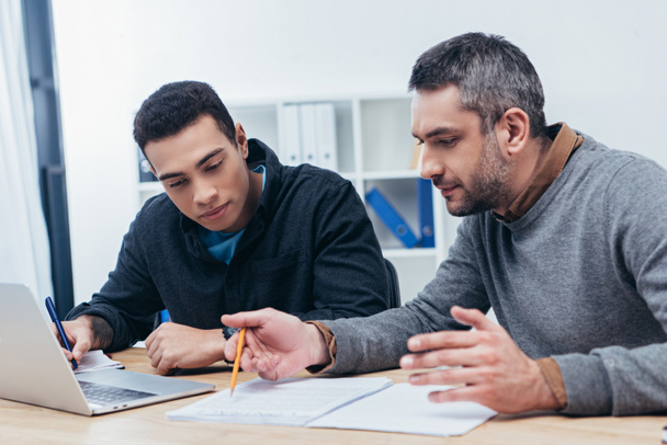 Konzentrierte männliche Mitarbeiter, die im Büro mit Papieren und Laptop arbeiten - Foto, Bild