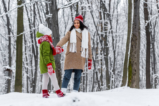 african american woman and preteen daughter walking, holding hands and looking at each other in winter park - Fotó, kép