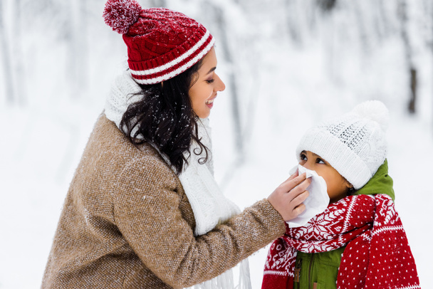 beautiful african american woman wiping with napkin nose of preteen daughter in winter park  - Photo, image