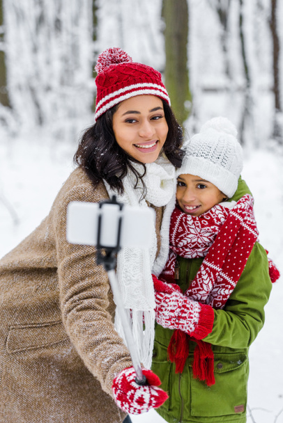 africano americano madre e hija en caliente ropa sonriendo y tomando selfie en invierno parque
 - Foto, Imagen