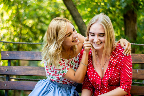 twee aantrekkelijke blonde vriendinnen praten en knuffelen in het park. Zusters hebben een goede tijd samen - Foto, afbeelding