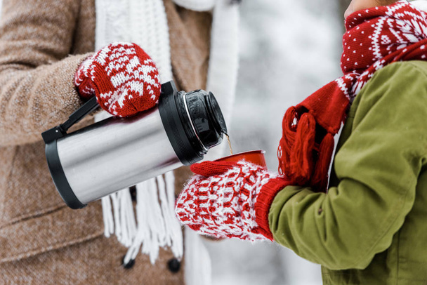 cropped view of woman pouring tea from thermos in red cup holding by child in winter - Photo, Image
