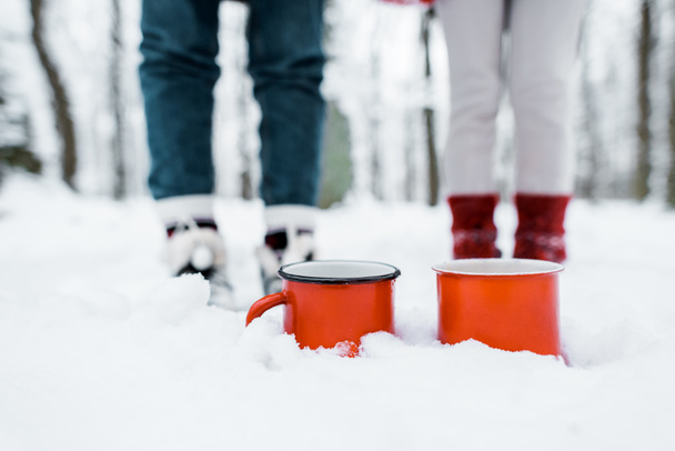 cropped view of red cups of tea staying in snow in park in snowy forest - Photo, image