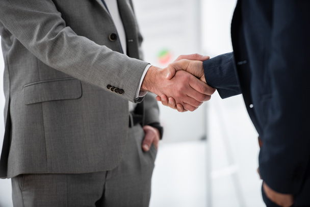 обрезанный снимок бизнесменов в формальной одежде пожимающих руки в офисе
   - Фото, изображение