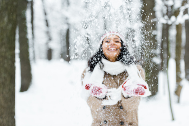 attractive african american woman throwing snow in park and smiling in winter forest - Photo, Image