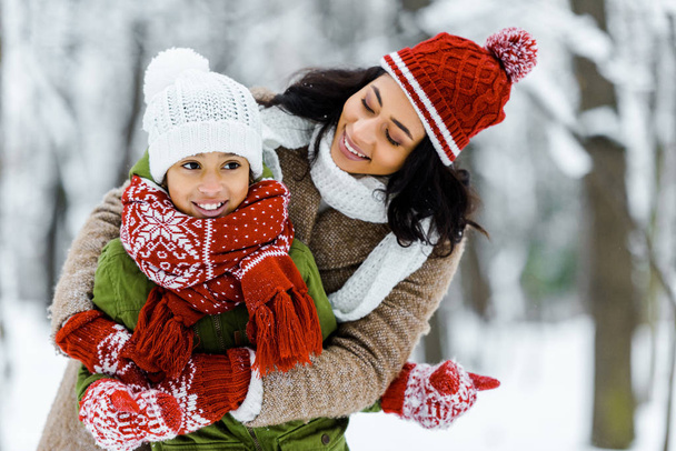 attractive african american mother hugging cute daughter in winter forest - Foto, immagini