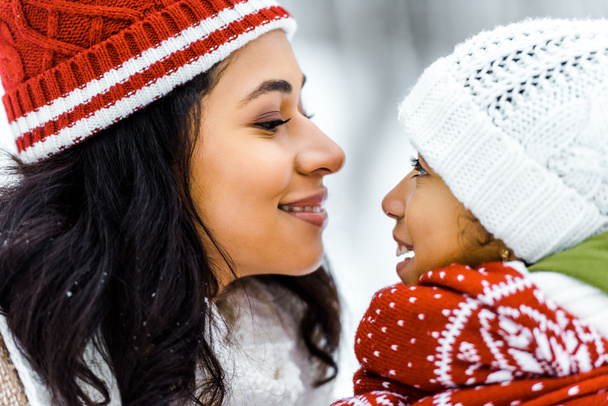 attractive african american mother smiling and looking at cute preteen daughter in winter forest - Photo, Image