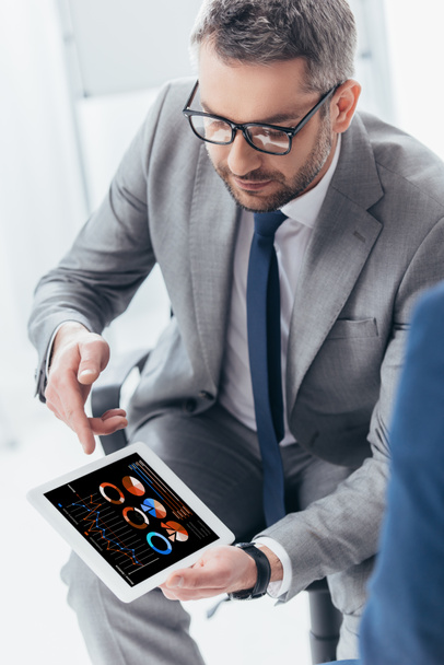 high angle view of handsome businessman in eyeglasses using digital tablet with business charts and graphs  - Foto, Imagem