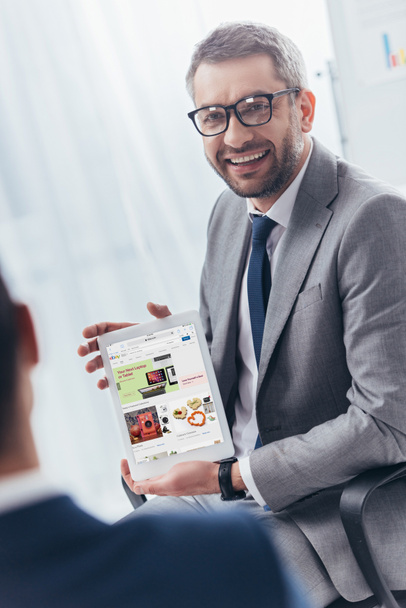 smiling businessman in eyeglasses holding digital tablet with ebay application on screen - Fotó, kép
