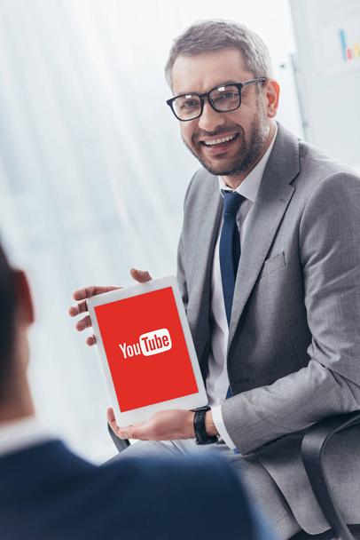 smiling businessman in eyeglasses holding digital tablet with youtube app on screen - Foto, Bild