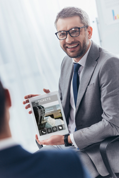 uśmiechający się biznesmen w okularach gospodarstwa cyfrowy tablet z bilety online aplikacji na ekranie - Zdjęcie, obraz