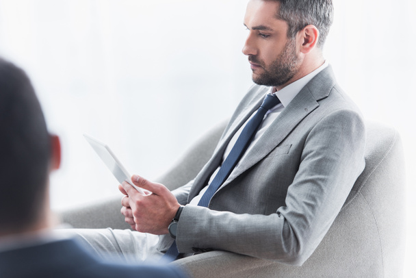 серьезный бородатый бизнесмен сидит и использует цифровой планшет в офисе
 - Фото, изображение