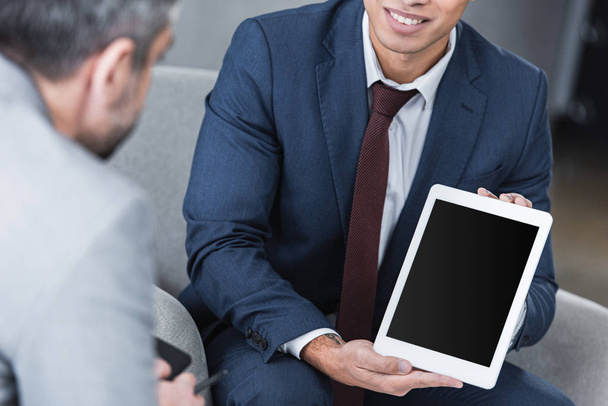 cropped shot of smiling young businessman showing digital tablet with blank screen to colleague          - Photo, Image