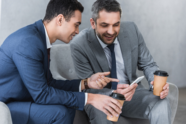 hymyilevä liikemiehet tilalla kahvia mennä ja käyttää älypuhelinta yhdessä
  - Valokuva, kuva