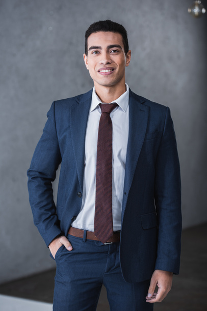 handsome young businessman standing with hand in pocket and smiling at camera - Fotografie, Obrázek