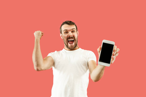 Young handsome man showing smartphone screen isolated on coral background in shock with a surprise face - Fotografie, Obrázek