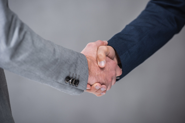 close-up partial view of businessmen shaking hands on grey - Foto, afbeelding