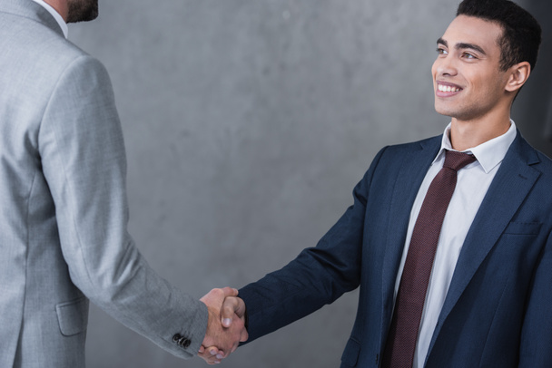 cropped shot of smiling young businessman shaking hands with colleague on grey - Foto, imagen