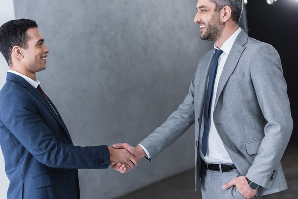 side view of businessmen shaking hands and smiling each other in office - Photo, Image