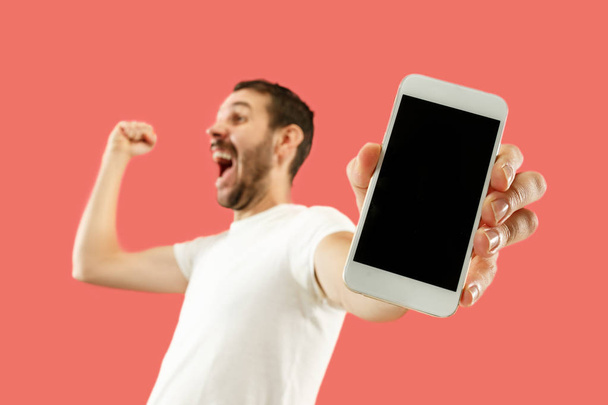 Young handsome man showing smartphone screen isolated on coral background in shock with a surprise face - Photo, Image