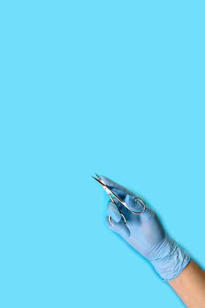 master nagels in blauwe handschoenen houdt manicure gereedschap. set van manicure accessoires op blauwe achtergrond bovenaanzicht. verticaal beeld. Samenstelling voor kaart met plaats voor tekst. - Foto, afbeelding